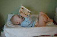 Alexandra reads a book while she gets a clean diaper